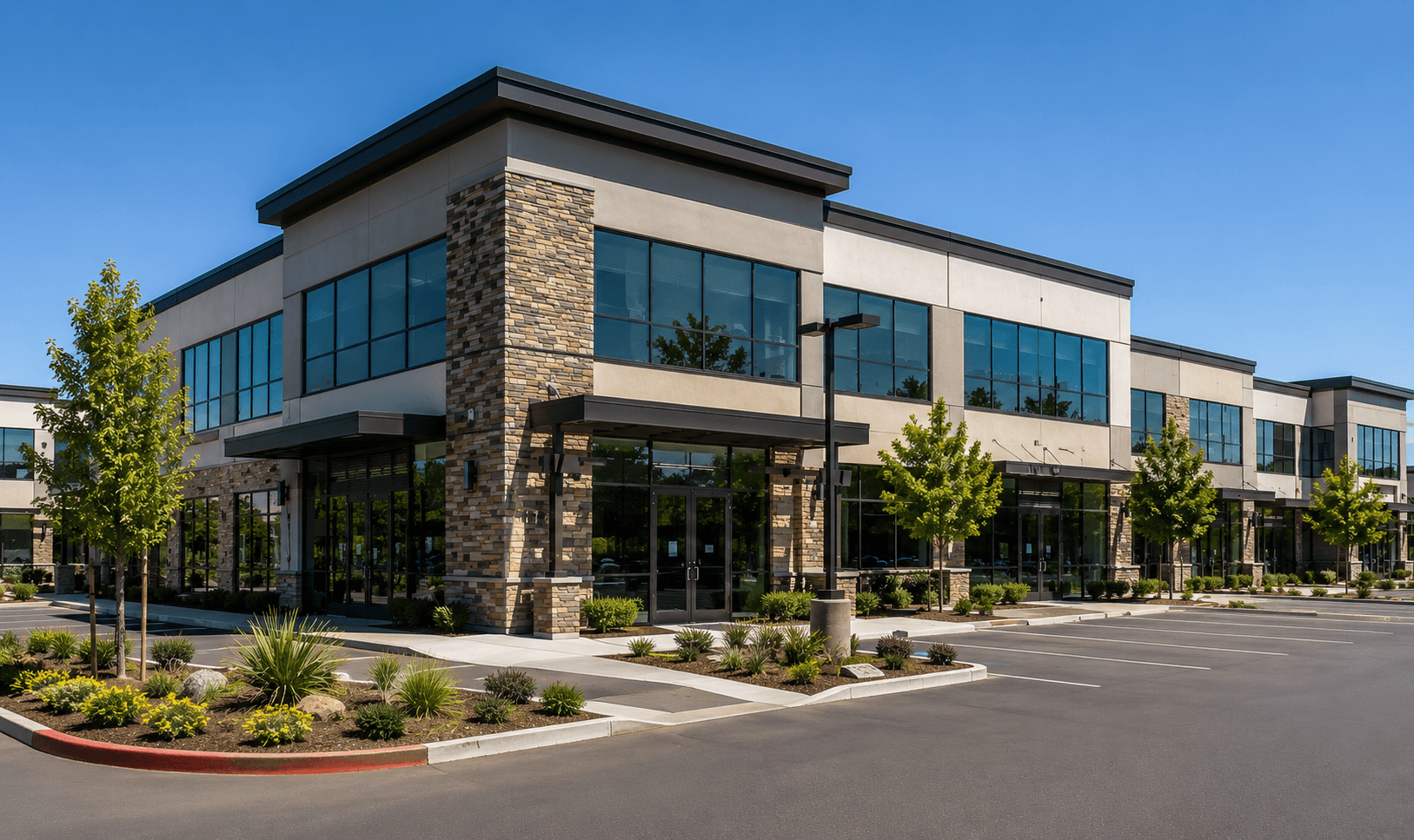 Modern commercial office building with glass storefronts, stone accents, landscaped grounds, and parking area in Sacramento, California.